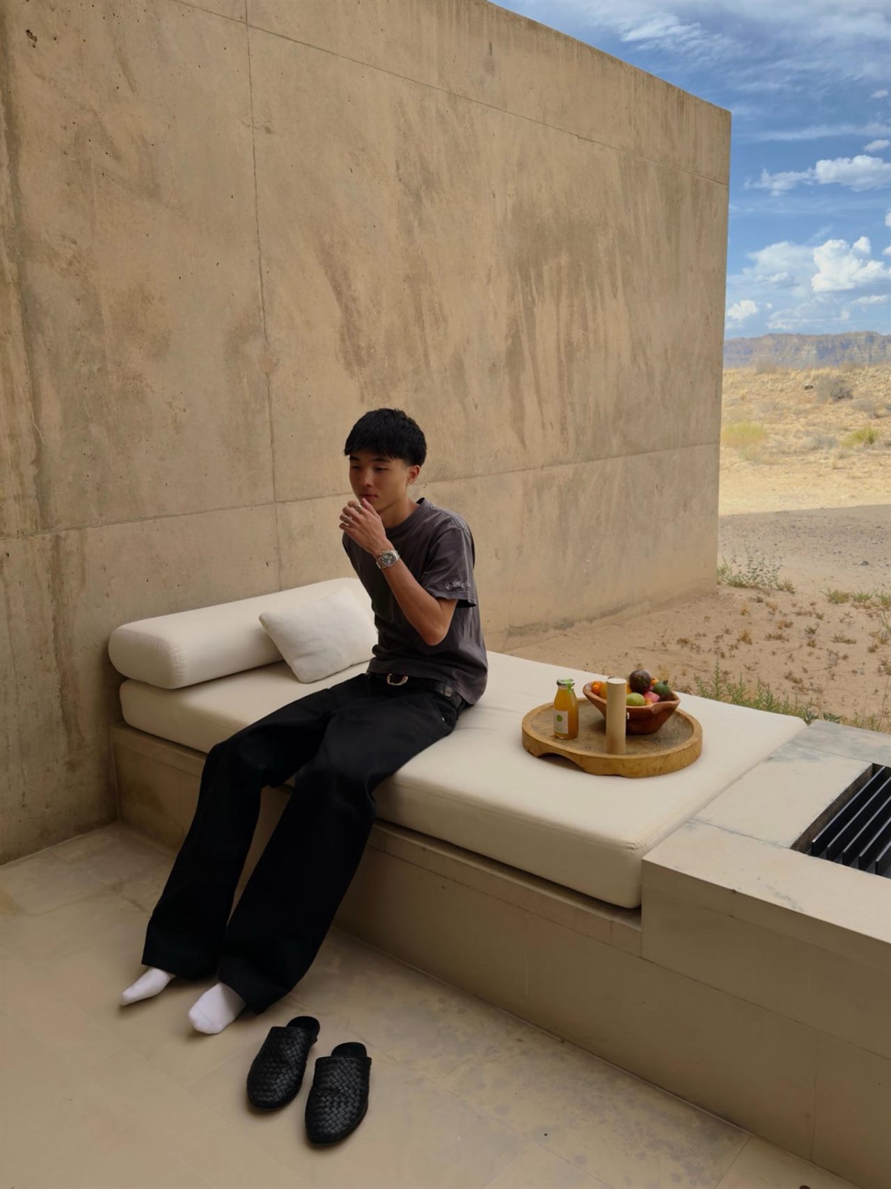 Clayton Kim seated on a daybed against a concrete wall, desert hills behind him