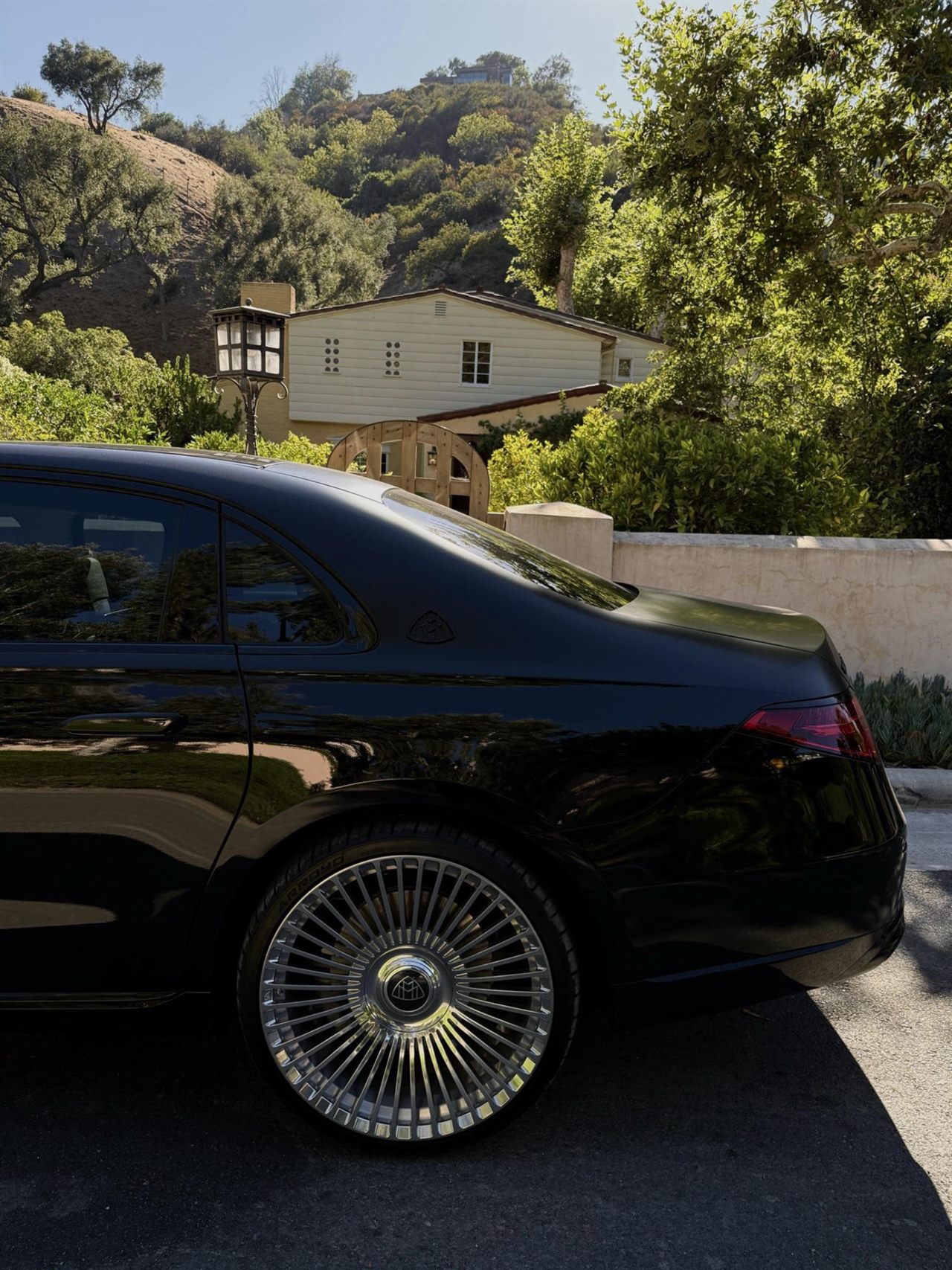 A black sedan parked below a pale house on a green canyon hill