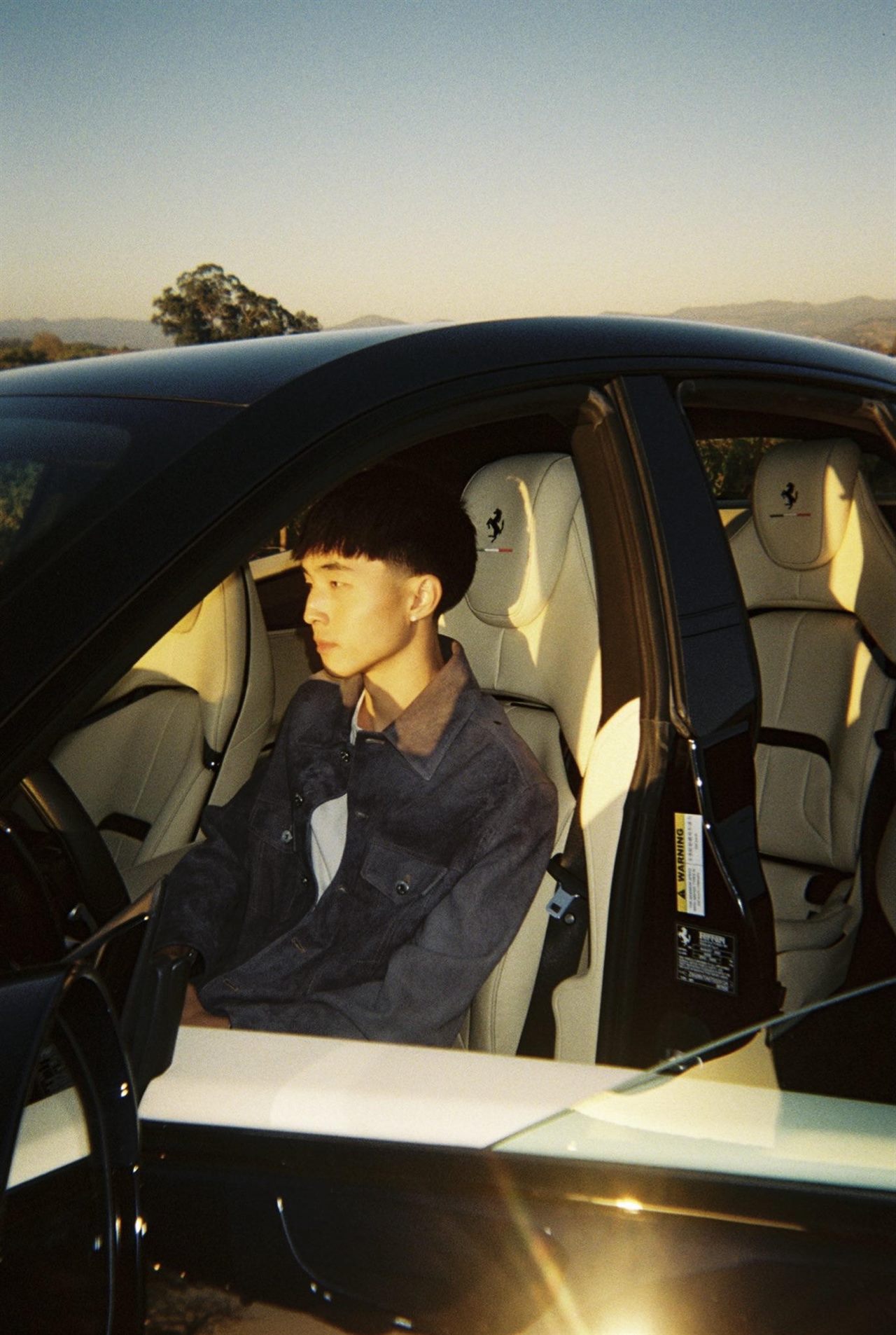 Clayton Kim in the driver’s seat of a black car, golden hour on the hills