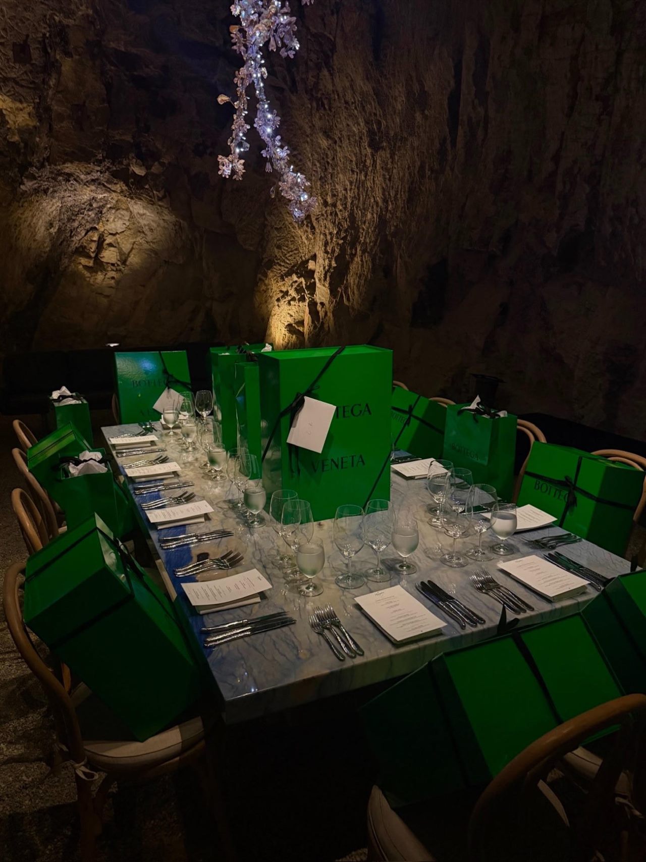 A long dinner table set inside a cave, green gift boxes at every place