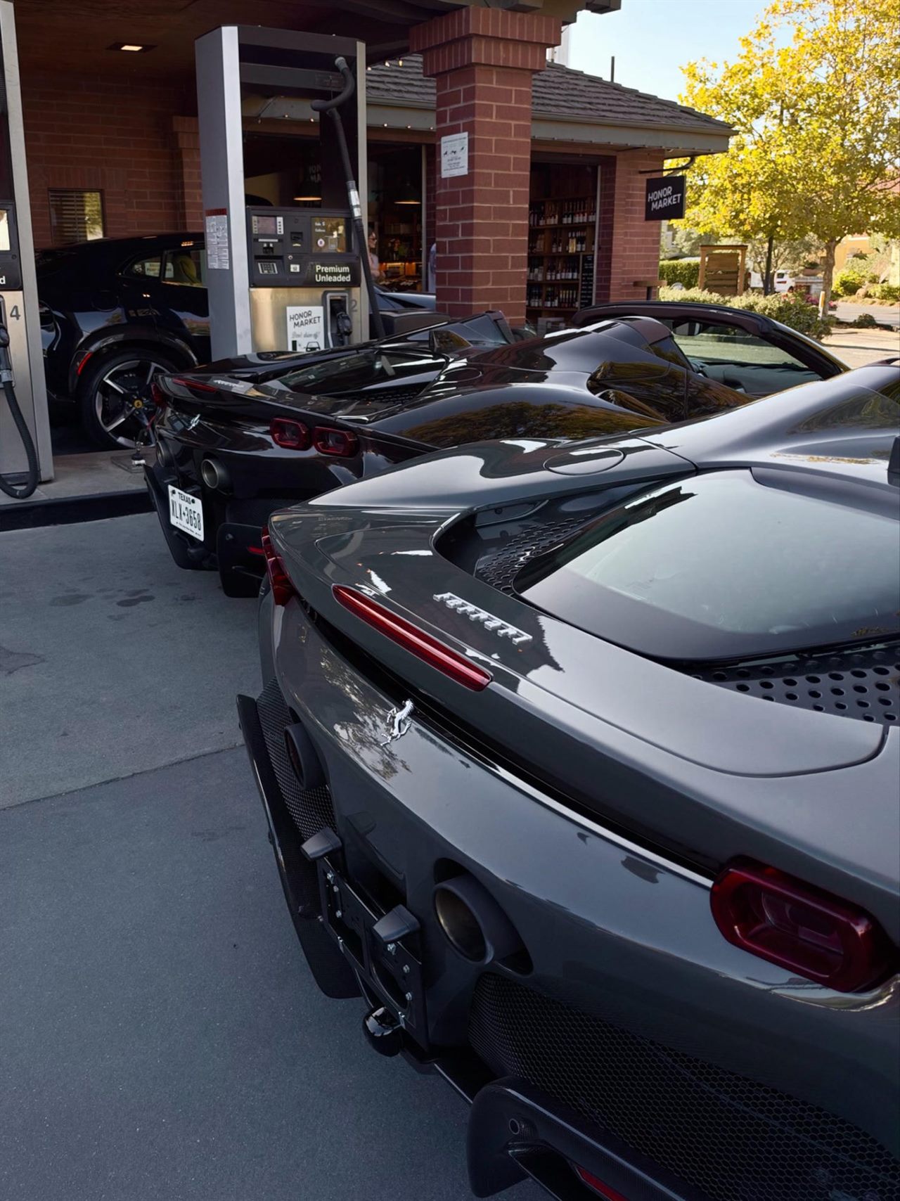 Two low sports cars stopped at a fuel pump in afternoon light