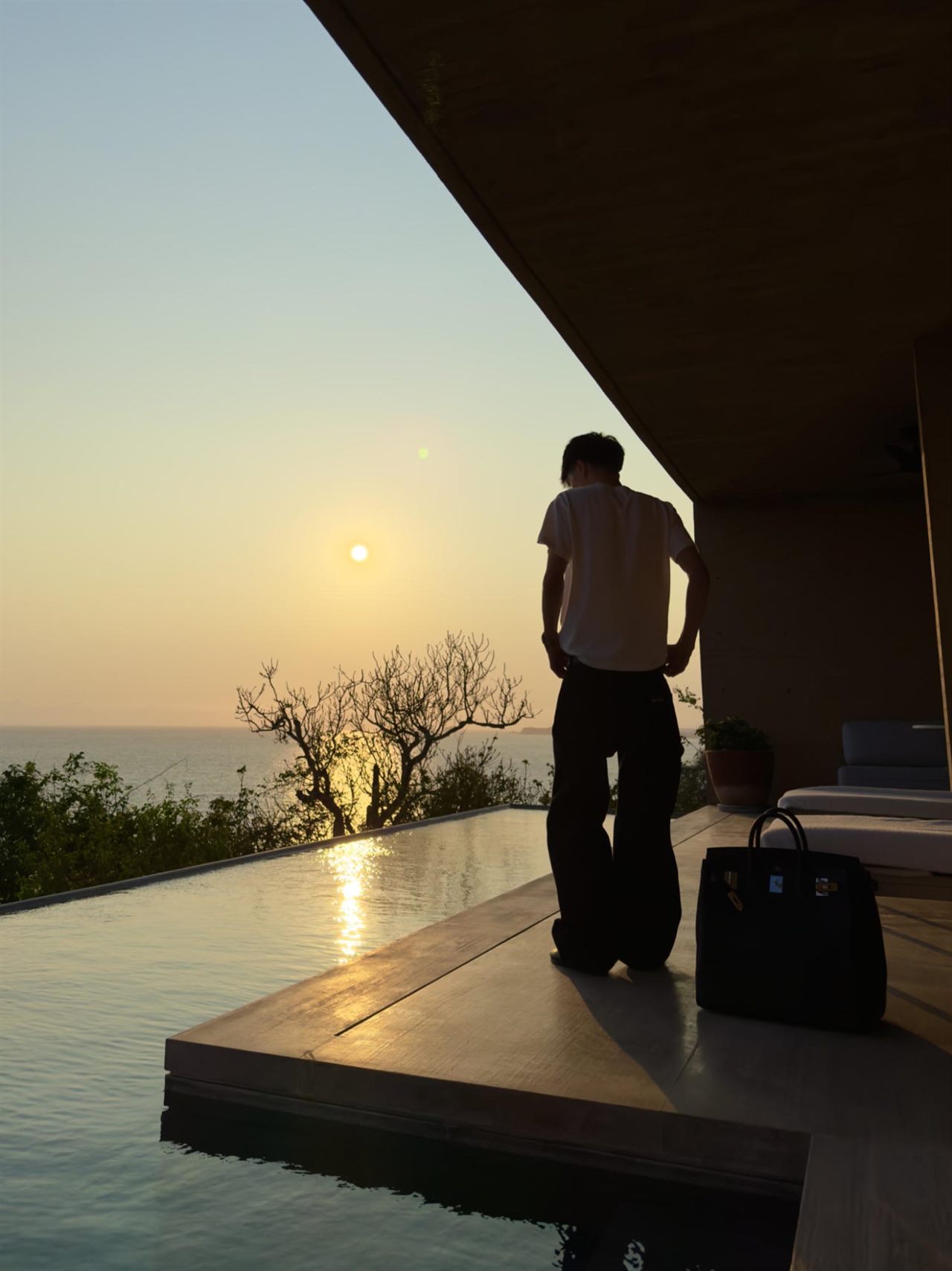 A silhouette at the edge of an infinity pool, the sun sitting on the sea